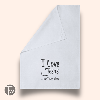 White cotton tea towel featuring the text "I Love Jesus ... but I cuss a little" in black script.