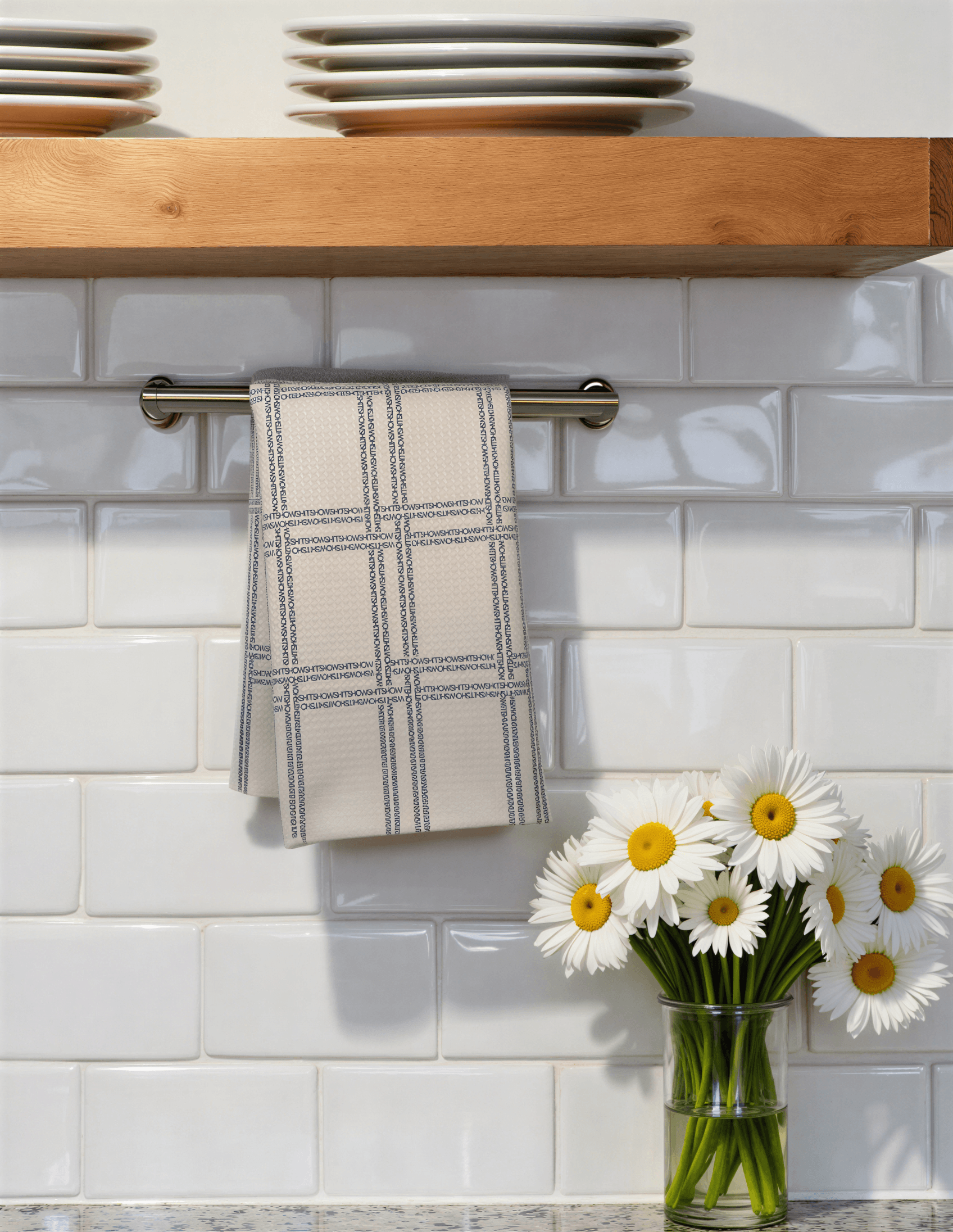 Shitshow plaid towel in retro colors hanging on a kitchen rack with white tiles and a vase of daisies nearby.