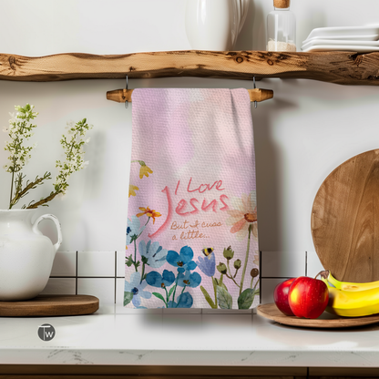 I Love Jesus but I cuss a little towel with floral design, hanging on a wooden shelf above kitchen items.
