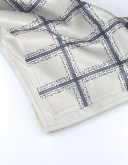 Fresh Out Plaid Illusion kitchen tea towel with a beige and navy plaid pattern, featuring textured fabric and a folded edge.