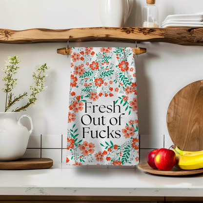 Fresh Out towel with floral design, hanging on a wooden shelf near a white pitcher and apples.