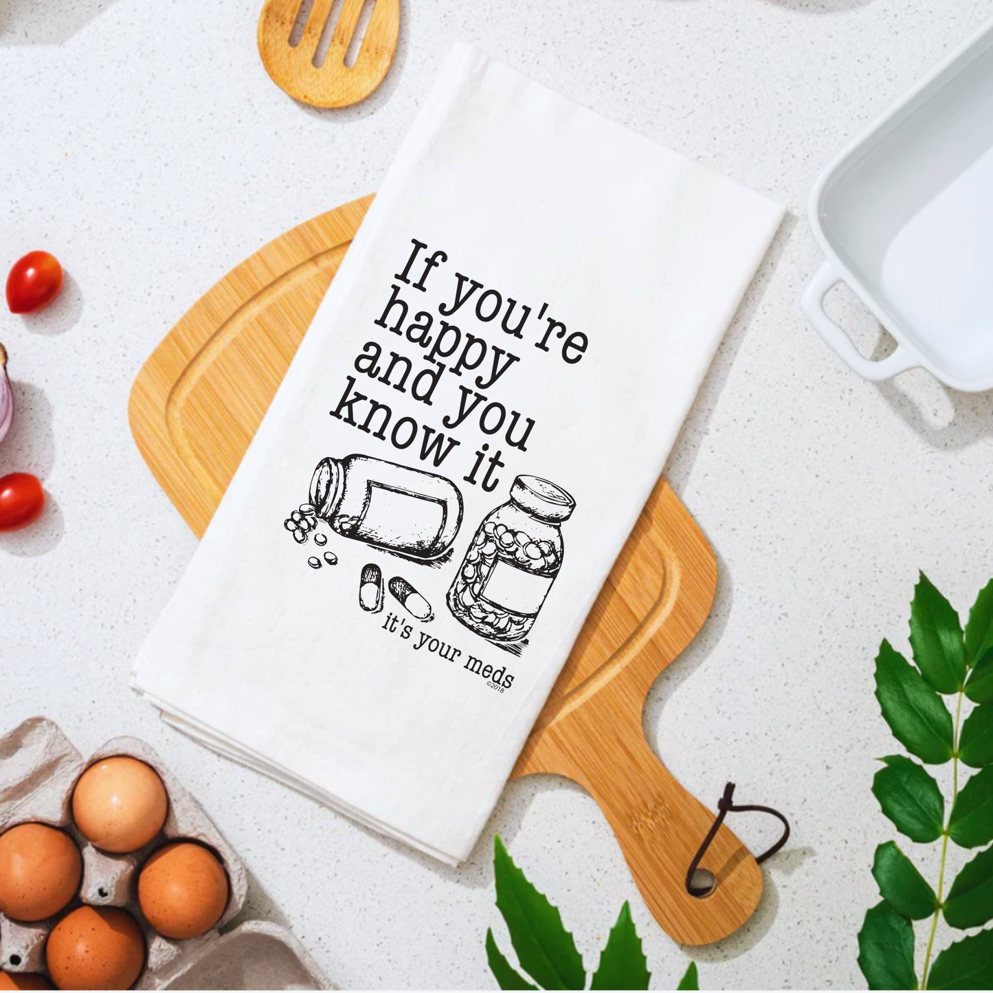 White cotton tea towel featuring the text "If you're happy and you know it, it's your meds" with illustrated pill bottles.
