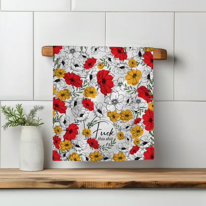 Floral towel featuring red, yellow, and black flowers with the text "Fuck this shit" on a wooden shelf.