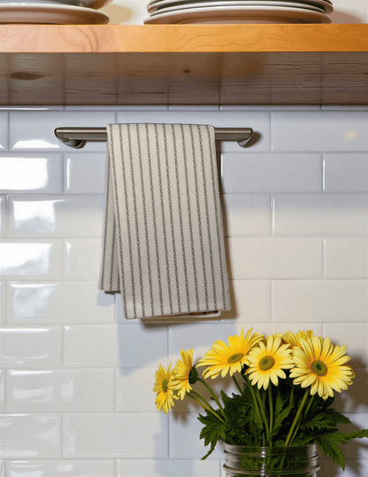 Shitshow in Colette stripes towel hanging on a rack above a white tiled backsplash with yellow flowers in a jar.
