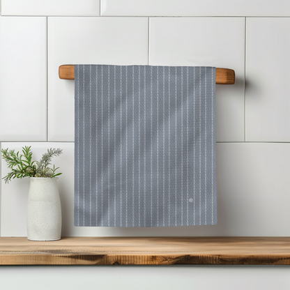 Colette Stripe Illusion towel hanging on a wooden rack, featuring light blue and white vertical stripes.