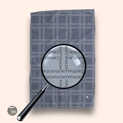 A gray plaid kitchen towel with a magnifying glass revealing repeated text pattern in bold black letters.