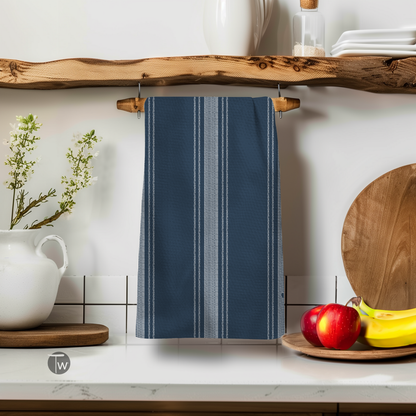 Dark blue Perfect Towel with white French stripes, hanging on a wooden shelf with decorative items and fruit.