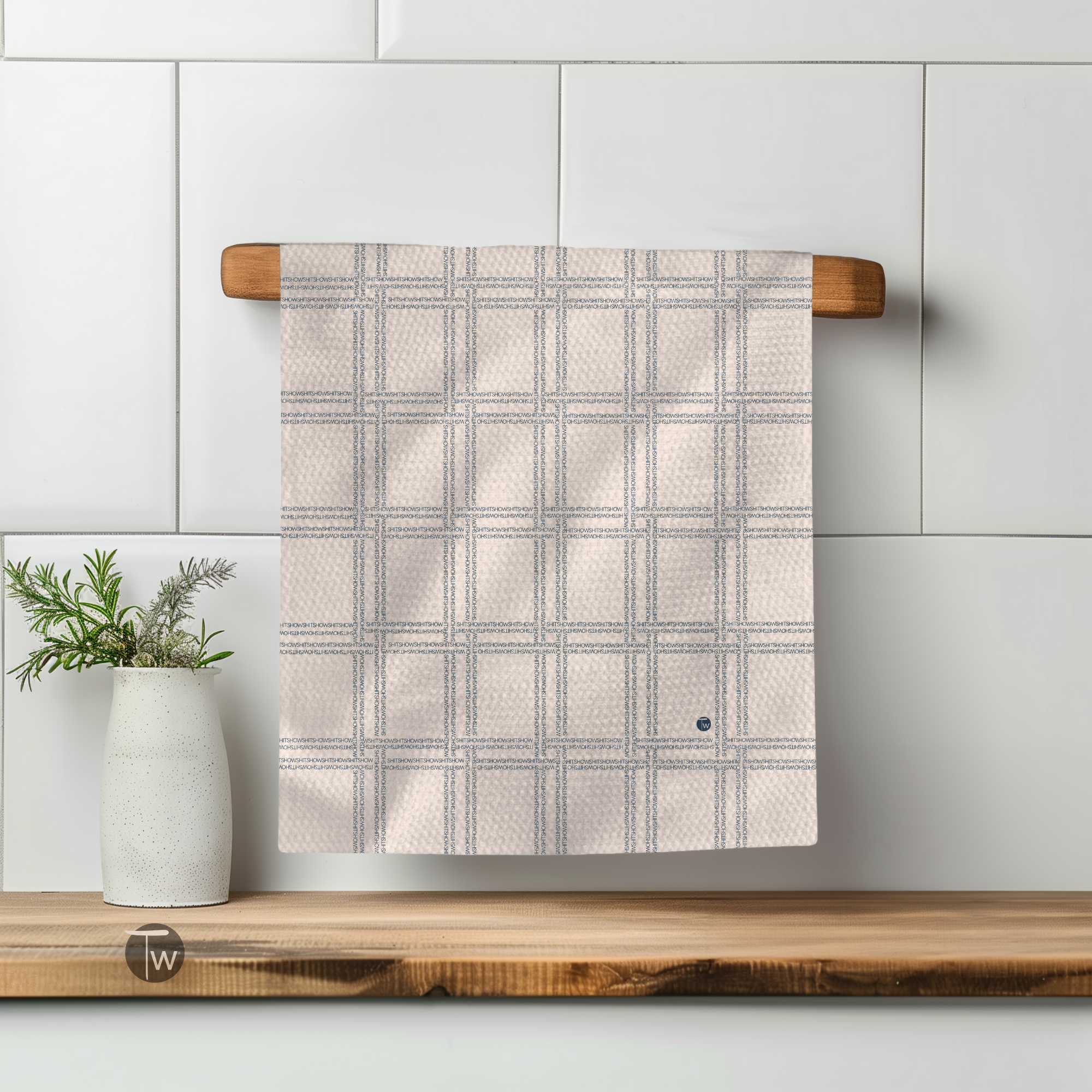Shitshow plaid towel in retro colors, hanging on a wooden rack with a white vase and plant nearby.