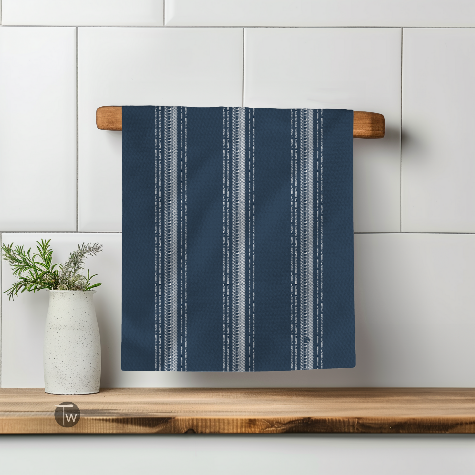 Dark blue Perfect Towel with French stripe design hanging on a wooden rack beside a white vase with greenery.