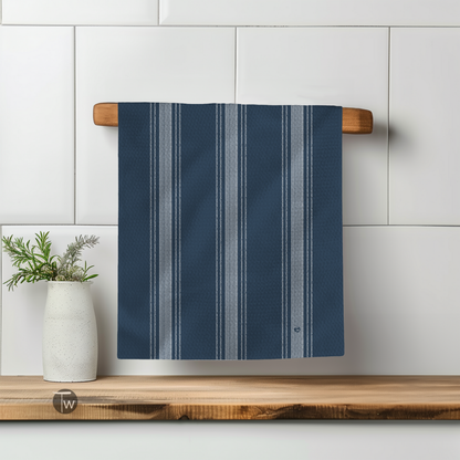 Dark blue Perfect Towel with French stripe design hanging on a wooden rack beside a white vase with greenery.