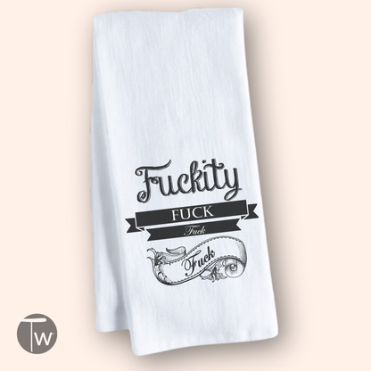 White cotton tea towel featuring the text "Fuckity Fuck" in black decorative font with a banner design.