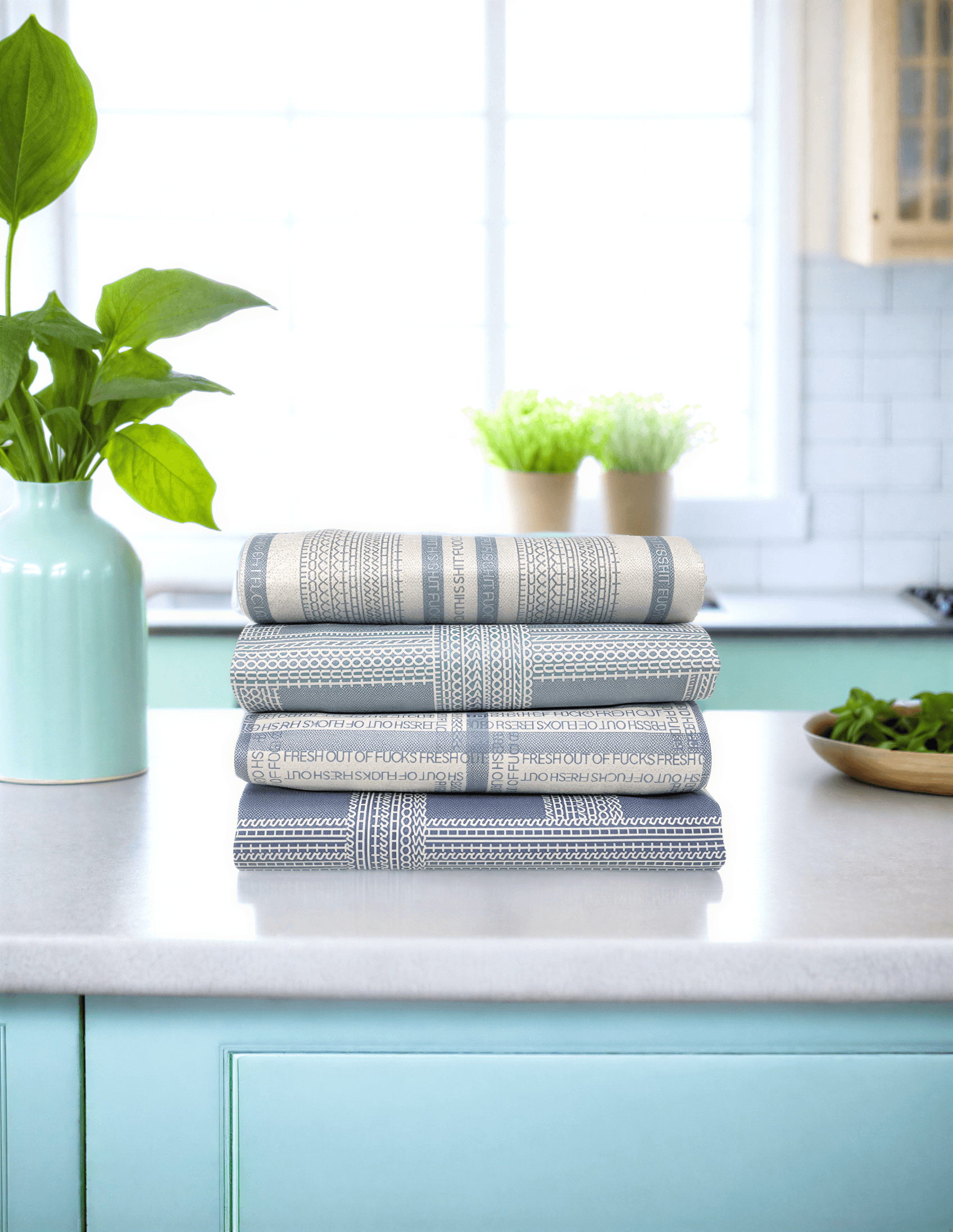 Vintage Shitshow Classic Illusion kitchen tea towel stacked in a kitchen with a mint green cabinet and plants.