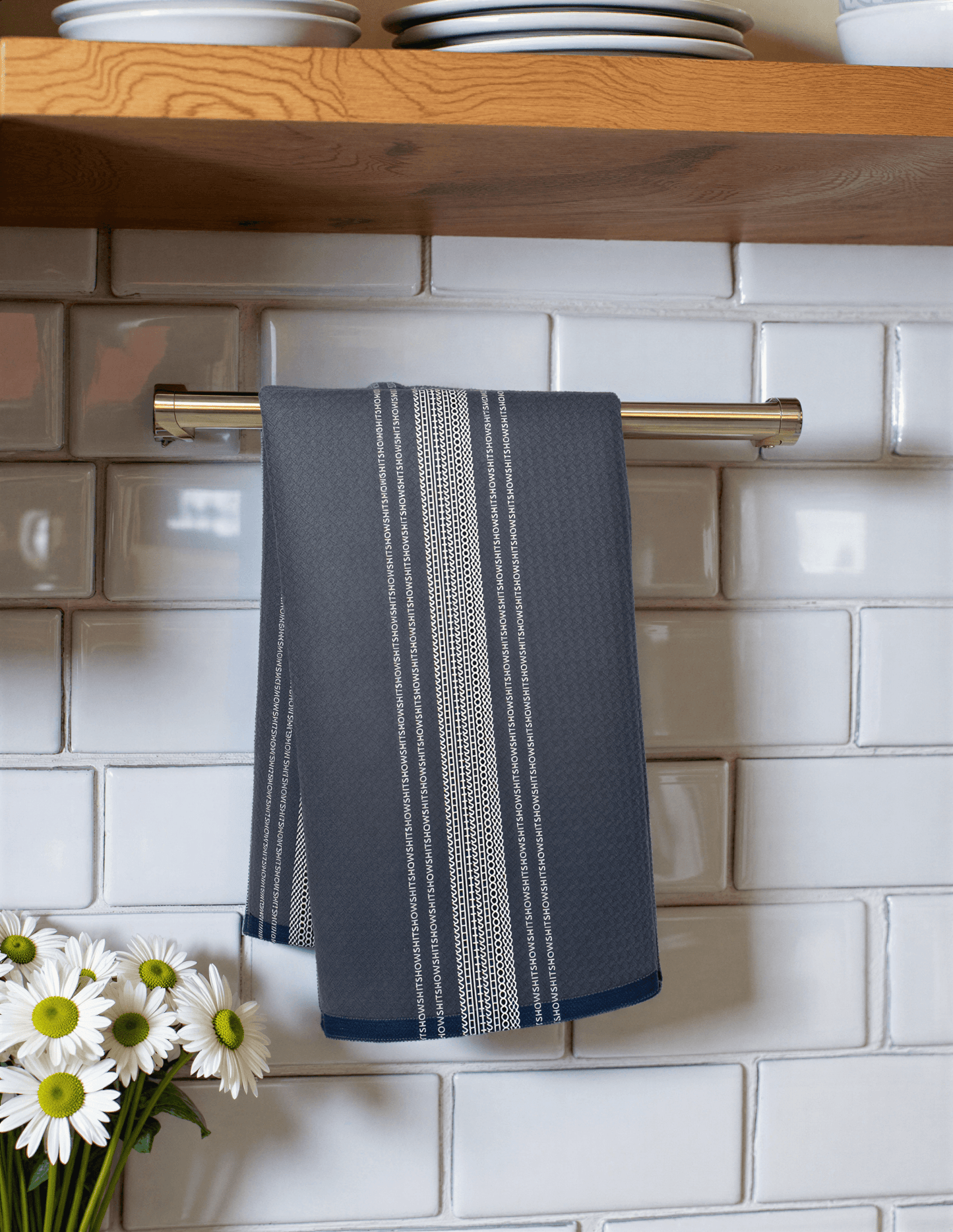 Dark blue towel with white French stripes hanging on a silver rack against a tiled wall, near a vase of daisies.