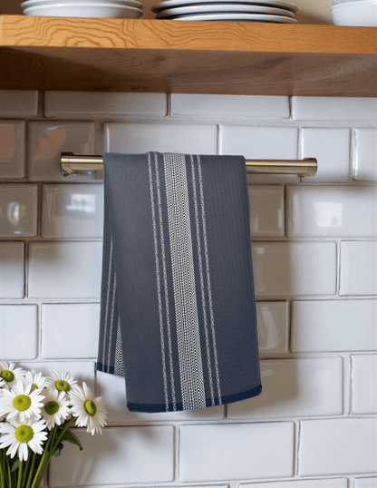 Dark blue towel with white French stripes hanging on a silver rack against a tiled wall, near a vase of daisies.